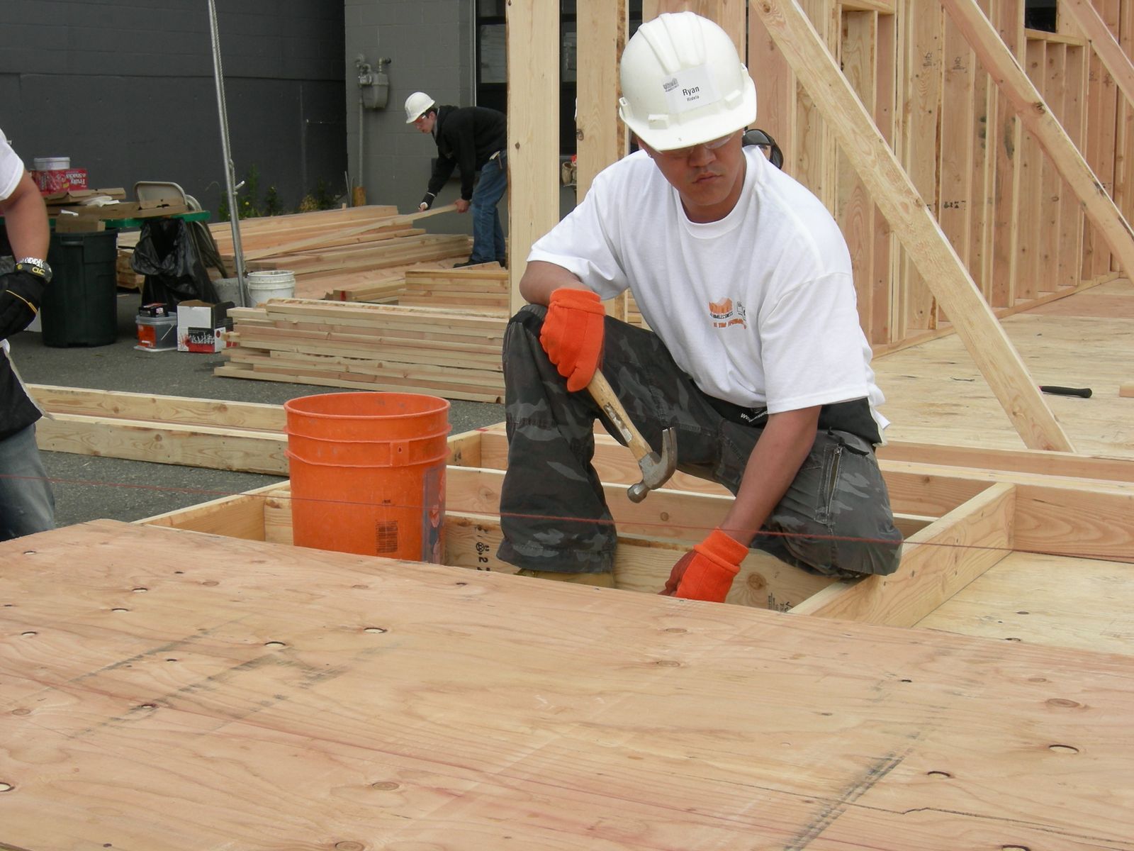 Carpenter in a hard hat nailing floor framing with a hammer