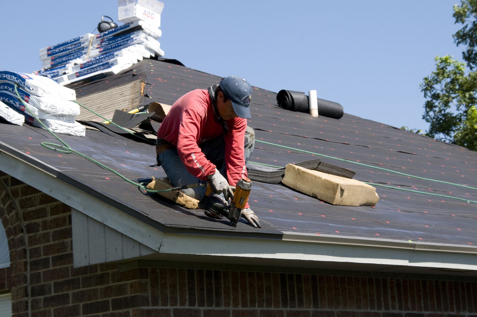 Roofer kneeling on underlayment driving nails with a nail gun